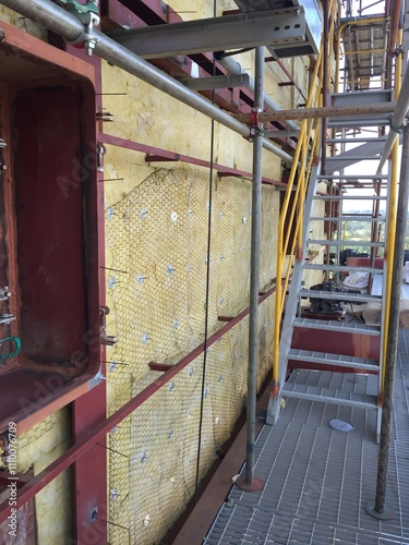 Scaffolding structure with insulation and chicken wire mesh on a construction site for thermal protection in industrial engineering.