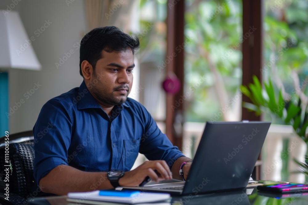 Fototapeta premium Portrait of handsome young indian man using laptop and earphone at home office