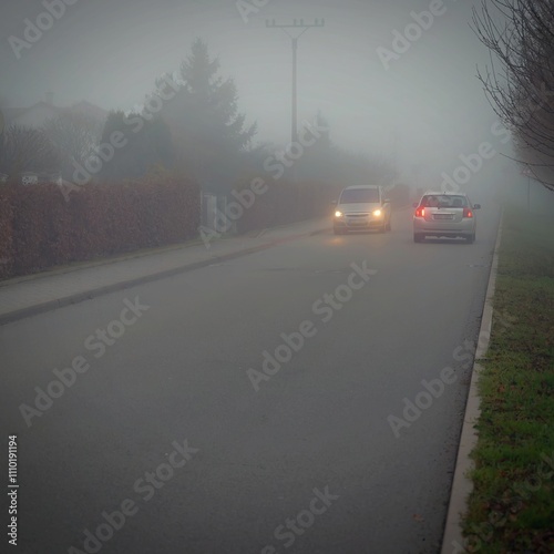 Car traveling on the foggy road with headlights or headlamps on. Low visibility - Dangerous driving of cars in winter in bad weather.