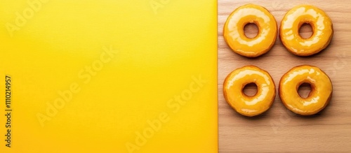 Orange glazed donuts arranged artistically on wooden plank with vibrant yellow background perfect for dessert or snack themed content.