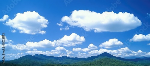 Serene summer landscape with blue skies and fluffy white clouds above lush green forests and majestic mountains.