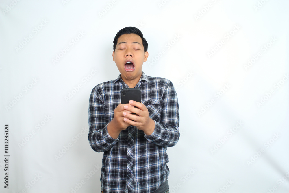 sleepy asian man holding mobile phone yawning feels tired isolated on white sleepy asian man holding mobile phone yawning feels tired isolated on white