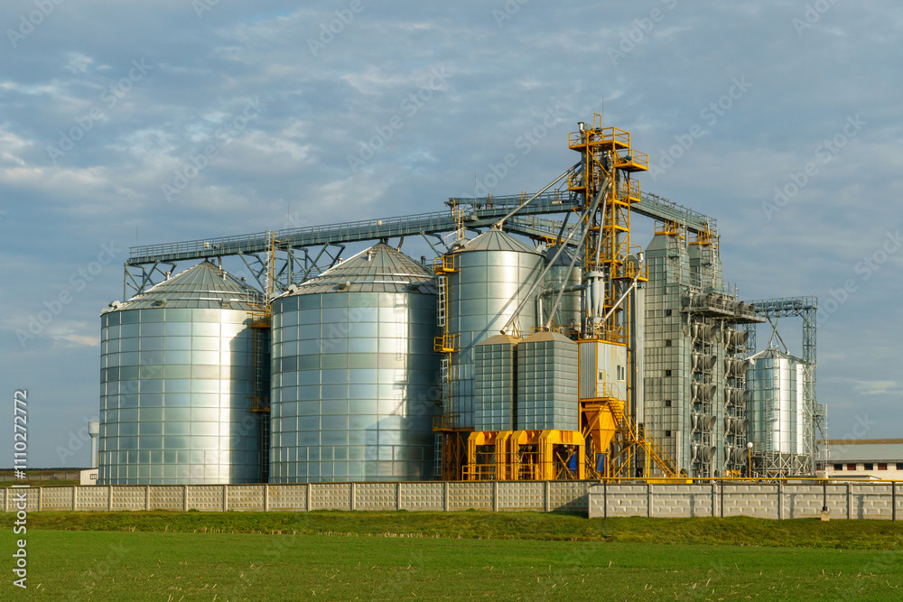 Silver silos in the field. A modern grain storage, processing and drying plant against the background of a sunset sky. Grain delivery and transportation. Silver silos in the field. A modern grain storage, processing and drying plant against the background of a sunset sky. Grain delivery and transportation.