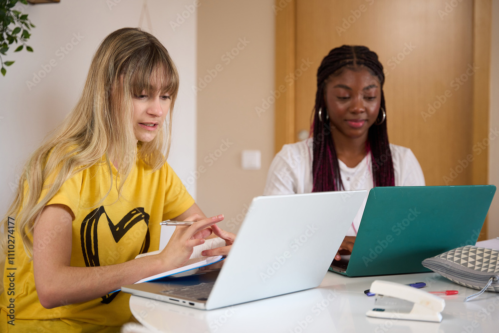 Multiethnic students studying together with laptops and notebooks at home Multiethnic students studying together with laptops and notebooks at home