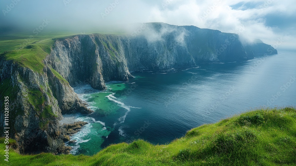 Fototapeta premium Rugged coastline with vibrant green hills under blue skies and misty clouds creating a serene natural landscape by the sea.