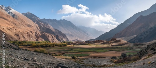 Panoramic view of majestic mountains surrounding ancient ruins in a serene valley landscape with lush fields and dramatic sky