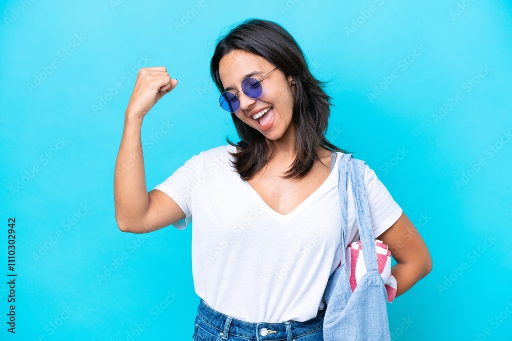 Fototapeta premium Young caucasian woman holding a beach bag isolated on blue background celebrating a victory