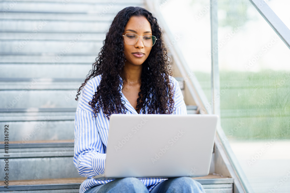A woman is working on her laptop while comfortably sitting on outdoor steps in sunlight A woman is working on her laptop while comfortably sitting on outdoor steps in sunlight