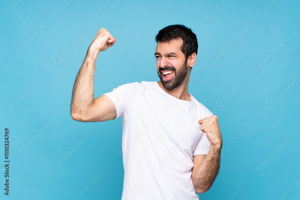 Young man with beard over isolated blue background celebrating a victory Young man with beard over isolated blue background celebrating a victory