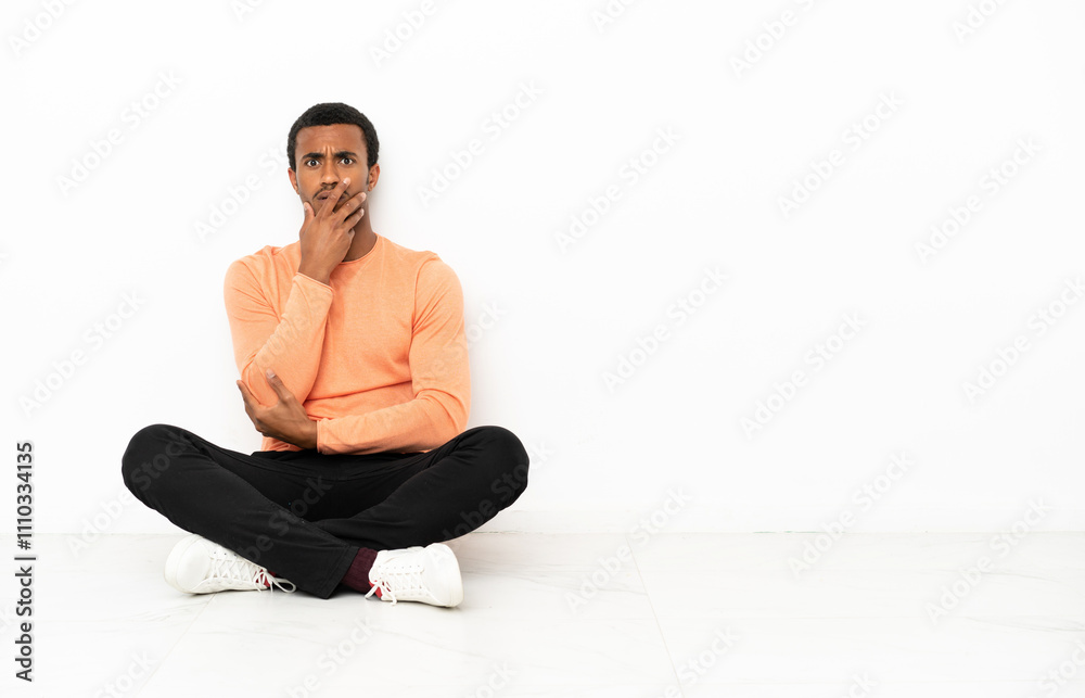 African American man sitting on the floor over isolated copyspace background surprised and shocked while looking right African American man sitting on the floor over isolated copyspace background surprised and shocked while looking right