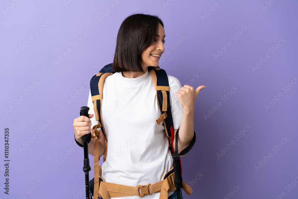 Young caucasian woman with backpack and trekking poles isolated on blue background pointing to the side to present a product Young caucasian woman with backpack and trekking poles isolated on blue background pointing to the side to present a product