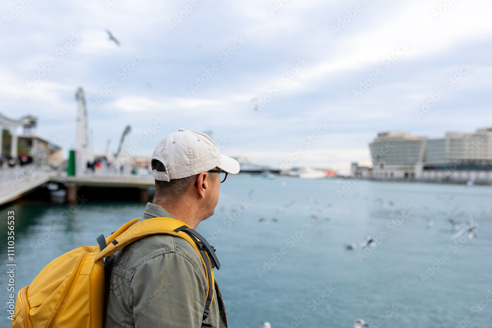 Tourist with yellow backpack strolling along the promenade of the port of Barcelona, Spain Tourist with yellow backpack strolling along the promenade of the port of Barcelona, Spain