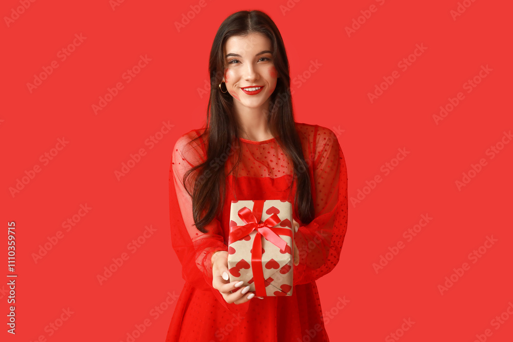 Beautiful young woman with kiss marks on her face and gift box on red background Beautiful young woman with kiss marks on her face and gift box on red background