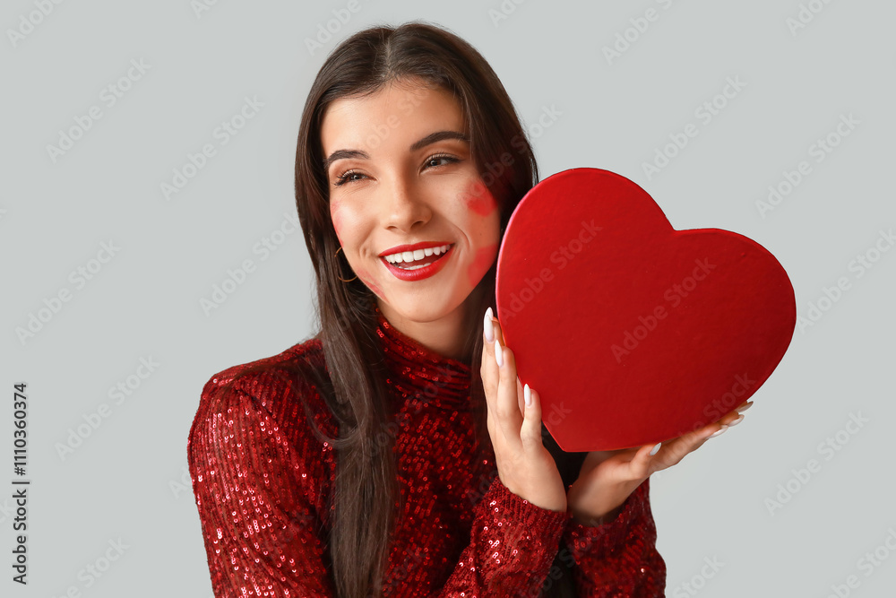 Happy young woman with kiss marks on her face and gift box on grey background Happy young woman with kiss marks on her face and gift box on grey background
