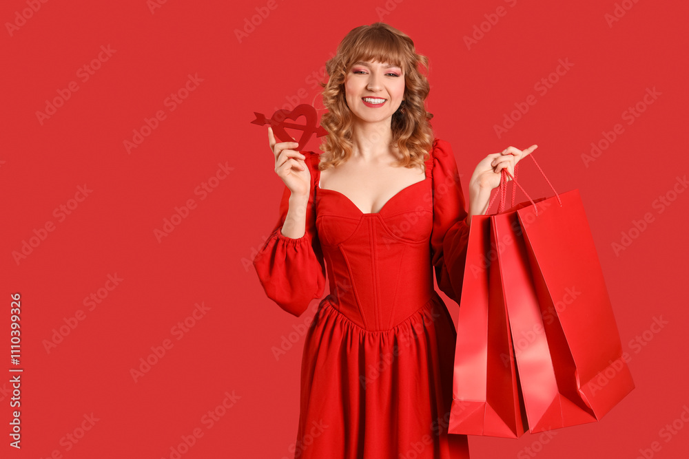 Beautiful young woman with shopping bags and heart on red background. Valentine's Day celebration Beautiful young woman with shopping bags and heart on red background. Valentine's Day celebration