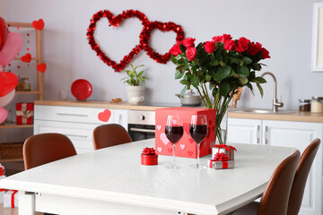 Dining table with bouquet of roses, wine glasses and gift boxes in light kitchen. Valentine's Day celebration