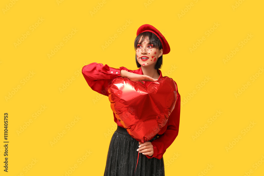 Beautiful young woman with creative makeup for Valentines Day and heart-shaped balloon on yellow background Beautiful young woman with creative makeup for Valentines Day and heart-shaped balloon on yellow background