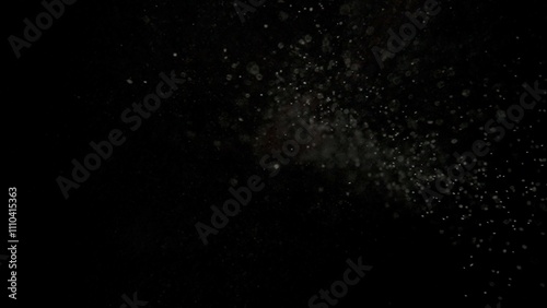 Many dust particles floating falling from top in light on empty black background with spotlight from above.