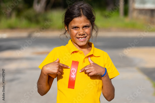 Aboriginal school girl pointing to second-place ribbon from athletics carnival pinned on her shirt