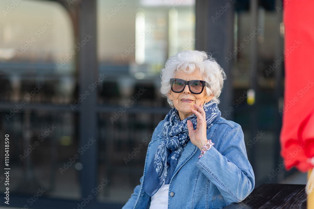 elderly lady wearing sunglasses with denim sitting with hand to face elderly lady wearing sunglasses with denim sitting with hand to face