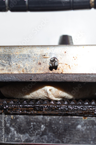 Obraz na płótnie The lower view of a panini press in operation, cooking a wrap to perfection. The photograph emphasizes the raw and industrial feel of the equipment and the food preparation process. w salonie
