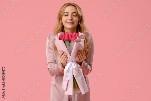 Portrait of beautiful middle-aged woman with bouquet of flowers on pink background. International Women's Day