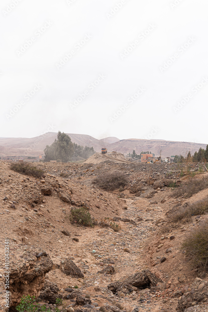 A desert road in southern Morocco, with cars and utility poles under an overcast sky.