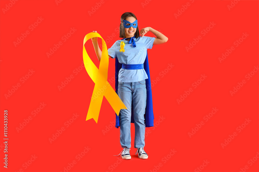 Fototapeta premium Little girl dressed as superhero with gold ribbon showing muscles on red background. Childhood cancer awareness concept