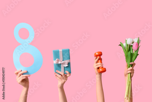 Female hands with paper figure 8, dumbbell, gift box and tulip flowers for International Women's Day on pink background