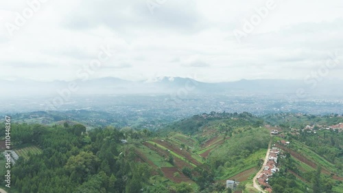 Aerial view of rice field, vegetable plantation, rural area in Dago near Lembang Fault, Bandung, West Java Indonesia revealing urban skyline cityscape southern mountain as background in dolly motion photo