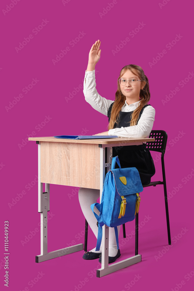 Cute girl with raised hand sitting at school desk on pink background Cute girl with raised hand sitting at school desk on pink background