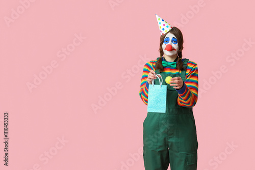 Young woman dressed as sad clown with shopping bag on pink background. April Fool's day celebration