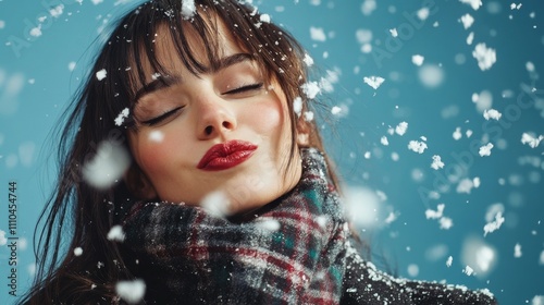 Brunette woman, fashion model, wearing plaid wool coat and scarf, smiling while surrounded by falling snow. Isolated against blue background. Winter fashion aesthetic.	