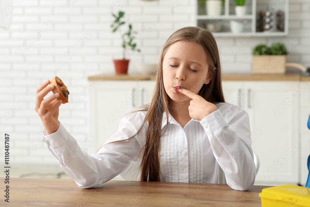 Cute little schoolgirl eating tasty nuts tart in kitchen at home Cute little schoolgirl eating tasty nuts tart in kitchen at home
