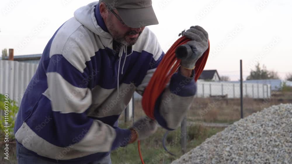 Adult man rolls up an electric wire.
Electrician. Construction work. Countryside plot. Open. Evening time. Real time. Adult man rolls up an electric wire.
Electrician. Construction work. Countryside plot. Open. Evening time. Real time.