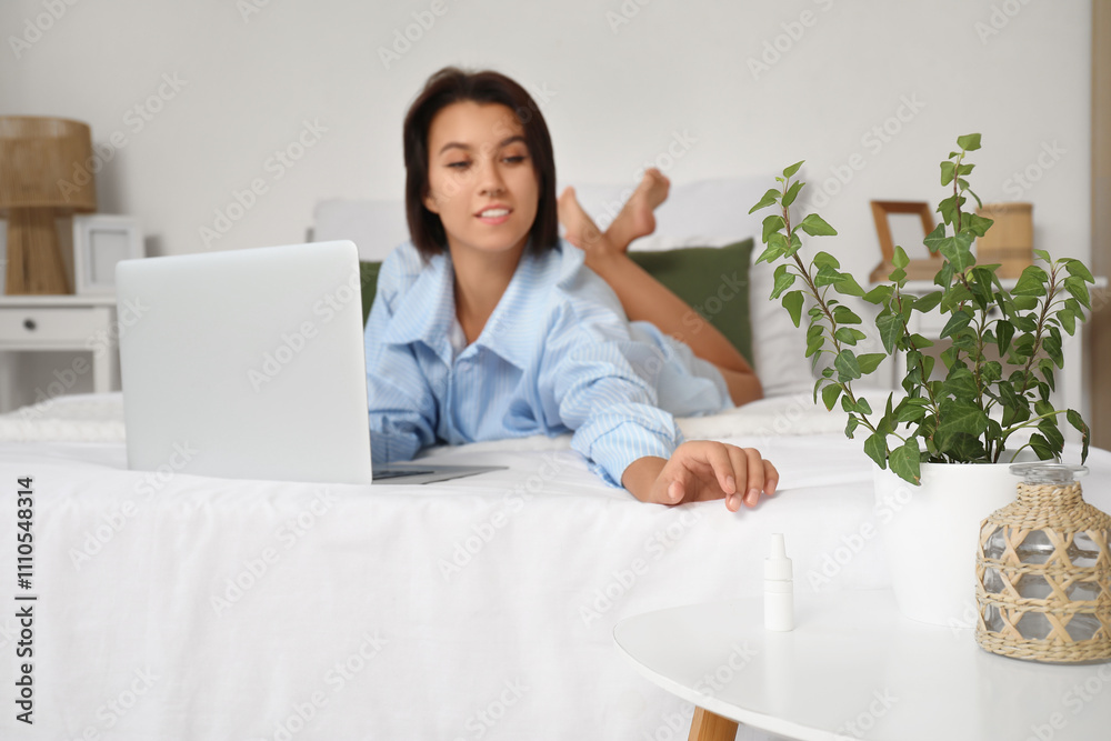Young woman with laptop taking eye drops from table in bedroom, closeup Young woman with laptop taking eye drops from table in bedroom, closeup