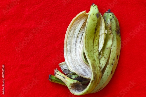 Discarded green robusta banana peel after picking fruits and banana pulp. Closeup macro top view of peeled ripe green bananas skin isolated on a red table background surface with copy space.
