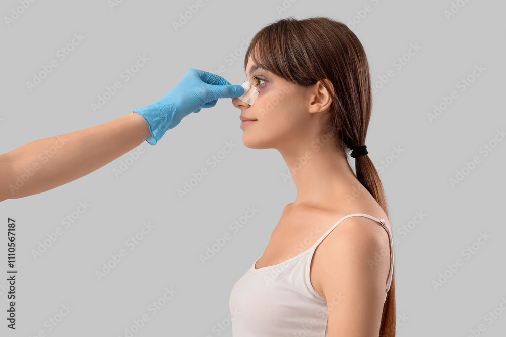 Surgeon hand touching woman's bandaged nose after plastic surgery on grey background Surgeon hand touching woman's bandaged nose after plastic surgery on grey background