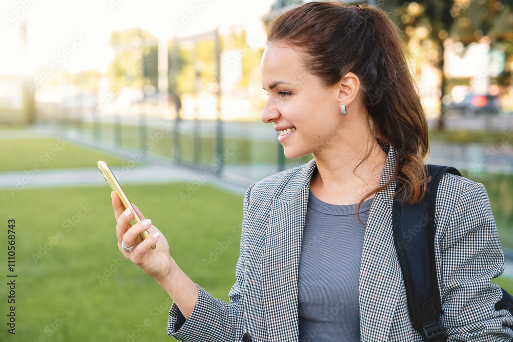 Caucasian businesswoman reading a message on her smartphone and smiling while standing on a city street. Caucasian businesswoman reading a message on her smartphone and smiling while standing on a city street.
