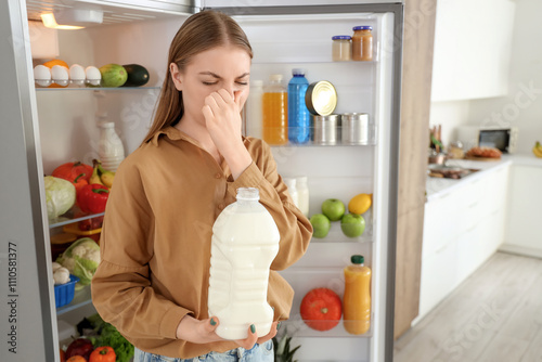 Young woman with spoiled milk near open fridge in kitchen