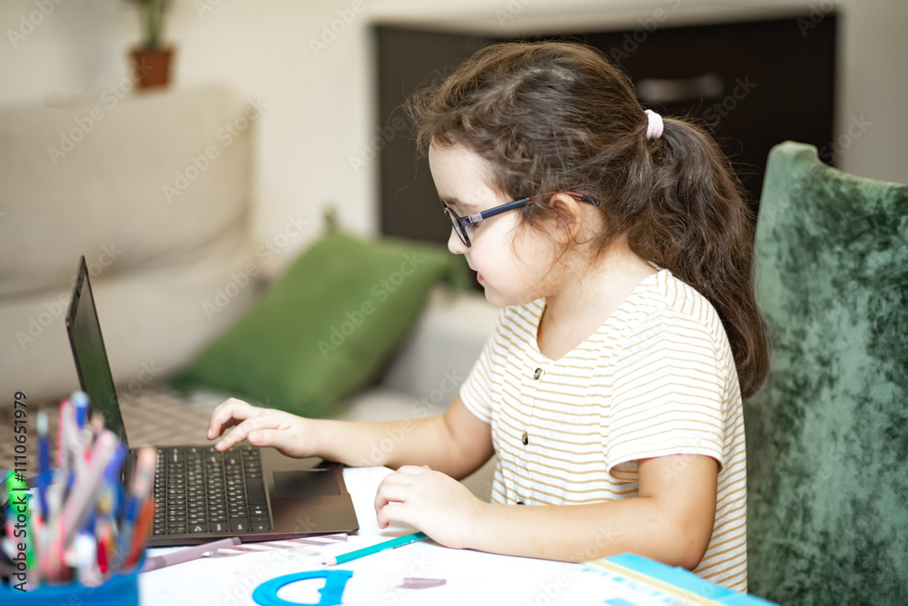 Little cute girl pupil at home making homework. Child studying online on laptop. Kid education. Little cute girl pupil at home making homework. Child studying online on laptop. Kid education.