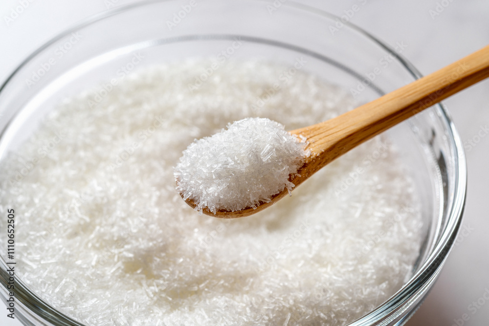 Monosodium glutamate in a wooden spoon over glass bowl full of MSG white crystals close-up. Concept of E621 flavor enhancer food additive. Monosodium glutamate in a wooden spoon over glass bowl full of MSG white crystals close-up. Concept of E621 flavor enhancer food additive.