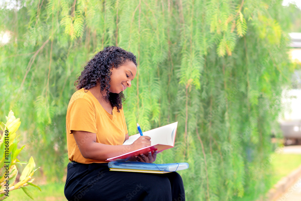 Jovem universitária negra brasileira escreve em seu caderno ao ar livre, sorrindo. Conquistou uma bolsa de estudos para a faculdade. Conceito de educação, superação e oportunidade Jovem universitária negra brasileira escreve em seu caderno ao ar livre, sorrindo. Conquistou uma bolsa de estudos para a faculdade. Conceito de educação, superação e oportunidade