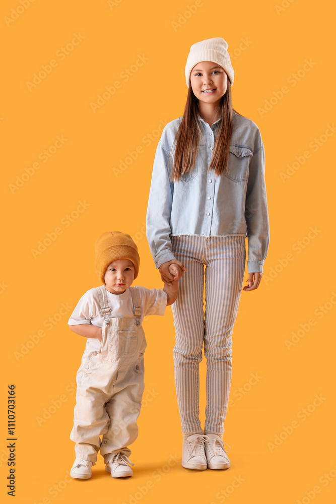 Teenage girl with her little brother holding hands on yellow background Teenage girl with her little brother holding hands on yellow background