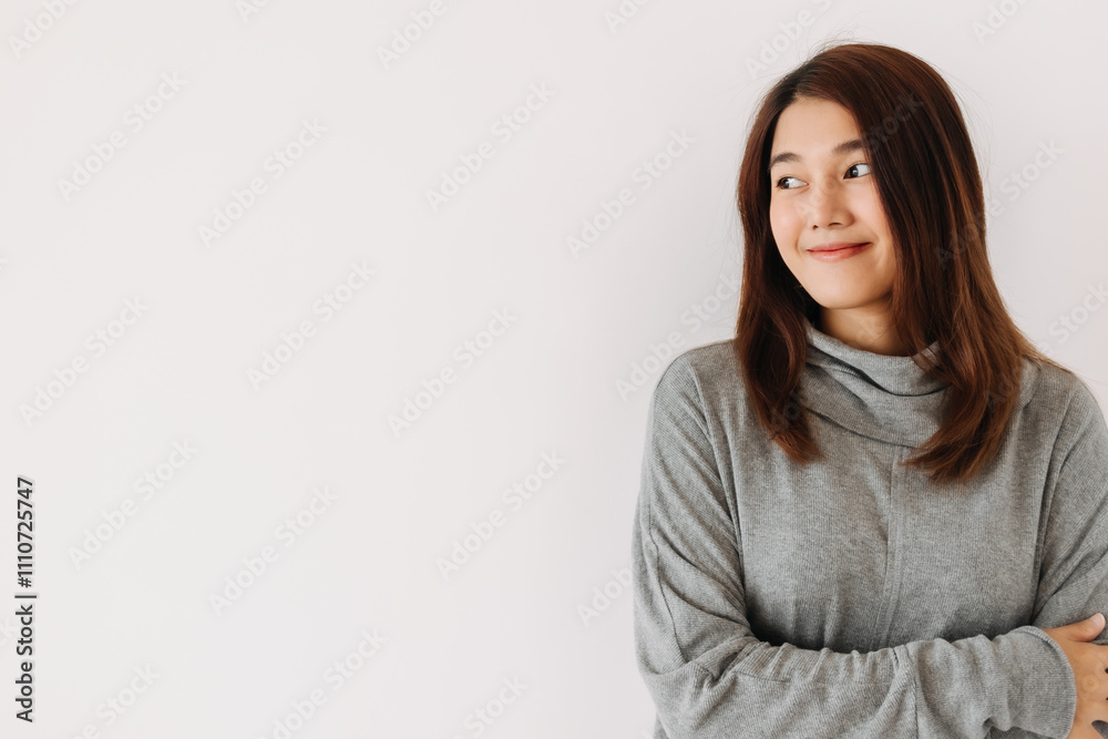 Happy beautiful asian Thai woman wear grey sweater, smiling and looking at empty space while standing isolated over white wall in winter. Happy beautiful asian Thai woman wear grey sweater, smiling and looking at empty space while standing isolated over white wall in winter.