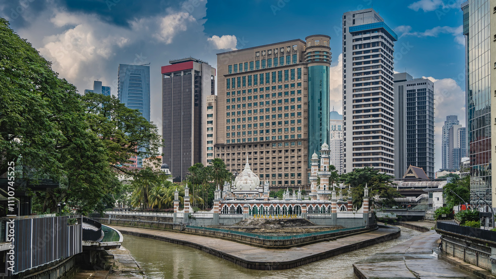 Naklejka premium The oldest Masjid Sultan Abdul Samad mosque at the confluence of the rivers. Weathered steps, galleries, arches. Domes and spires against the modern city skyscrapers. Blue sky, clouds. Kuala Lumpur.