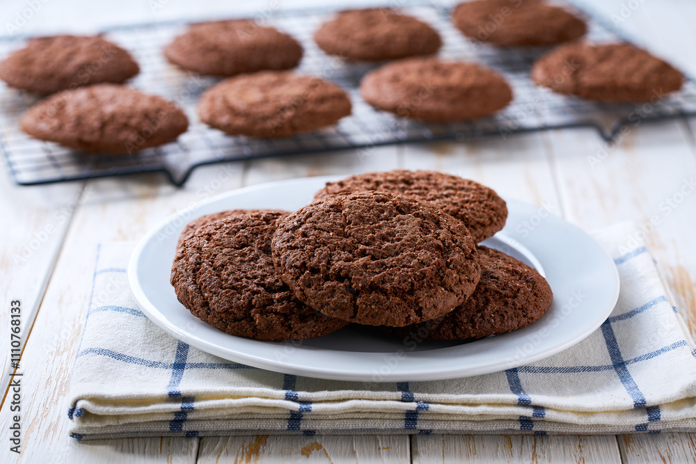 chocolate brownie cookies with cracks are cooling after baking on a rack on a white table, selective focus. chocolate brownie cookies with cracks are cooling after baking on a rack on a white table, selective focus.