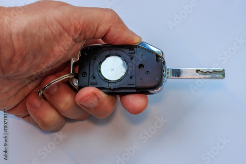 A man’s hand is holding a car key with the battery slot open, placed against a white background. The process of replacing the battery in an automatic car key.