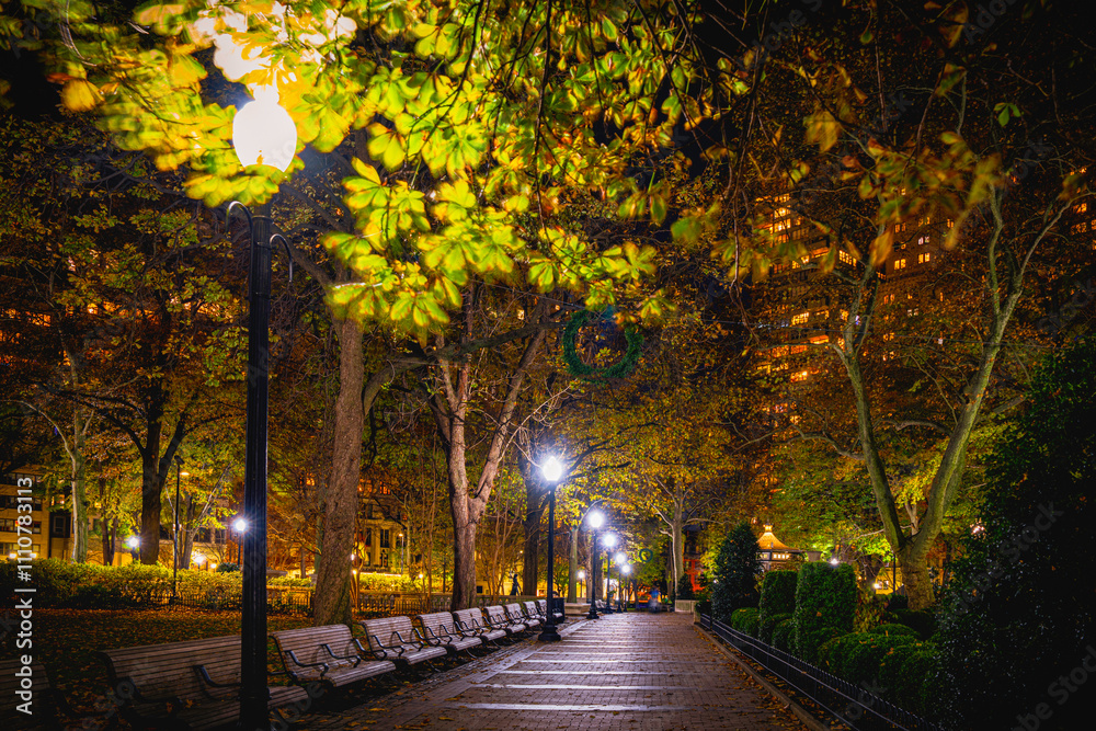 Naklejka premium Philadelphia City Public Park at Night: A quiet lighted resting space with autumn foliage on the pedestrian footpath in a metropolis of America in Pennsylvania