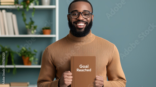 man proudly holds notebook celebrating his goals achieved in Q1. His smile reflects satisfaction and determination in cozy, plant filled environment photo